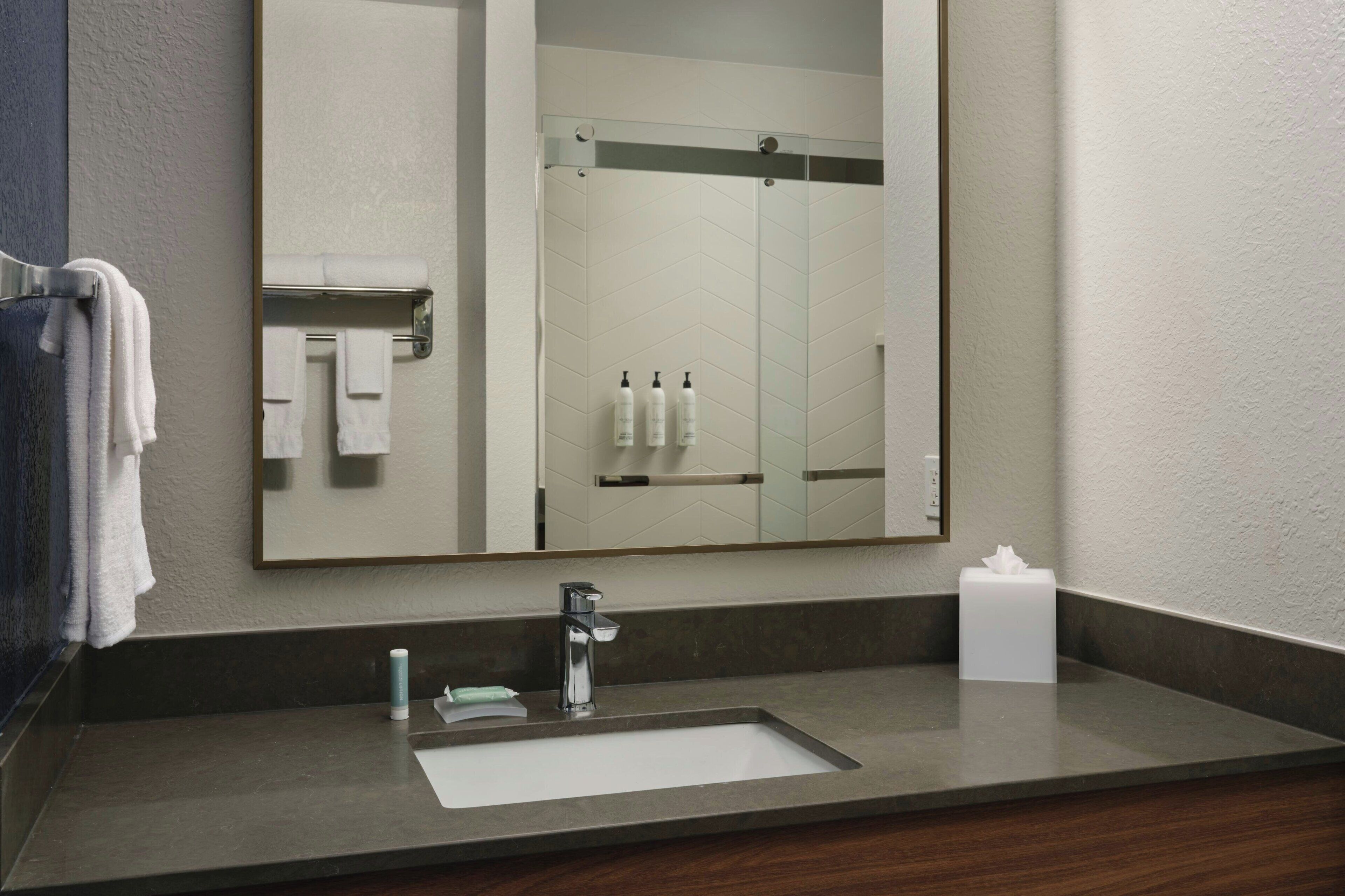 A bathroom with a sink, mirror, towel rack, and toiletries.
