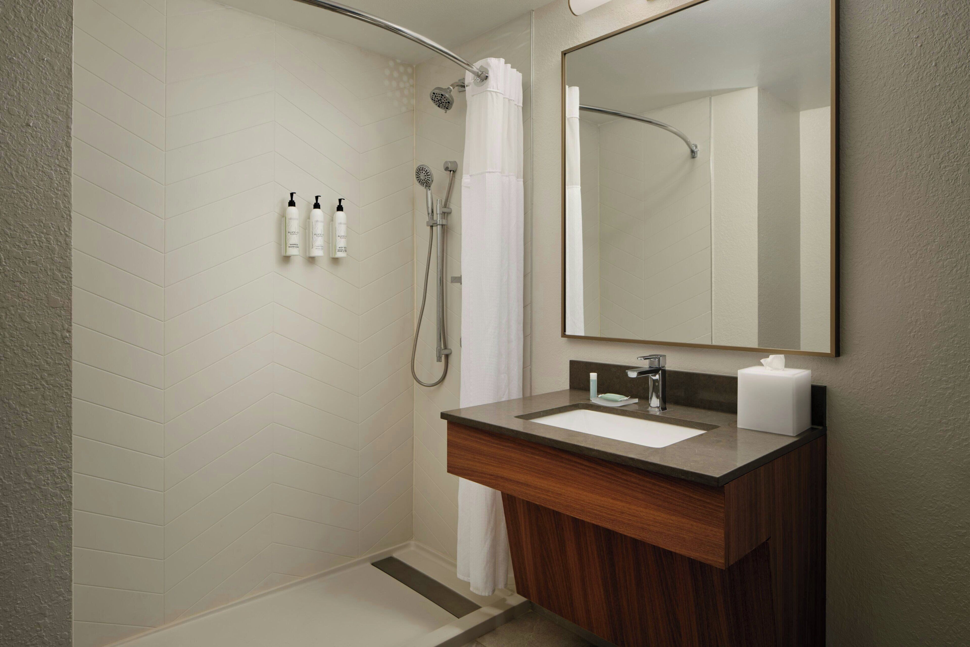 A modern bathroom with a shower, a sink with a mirror, and toiletries on the wall.