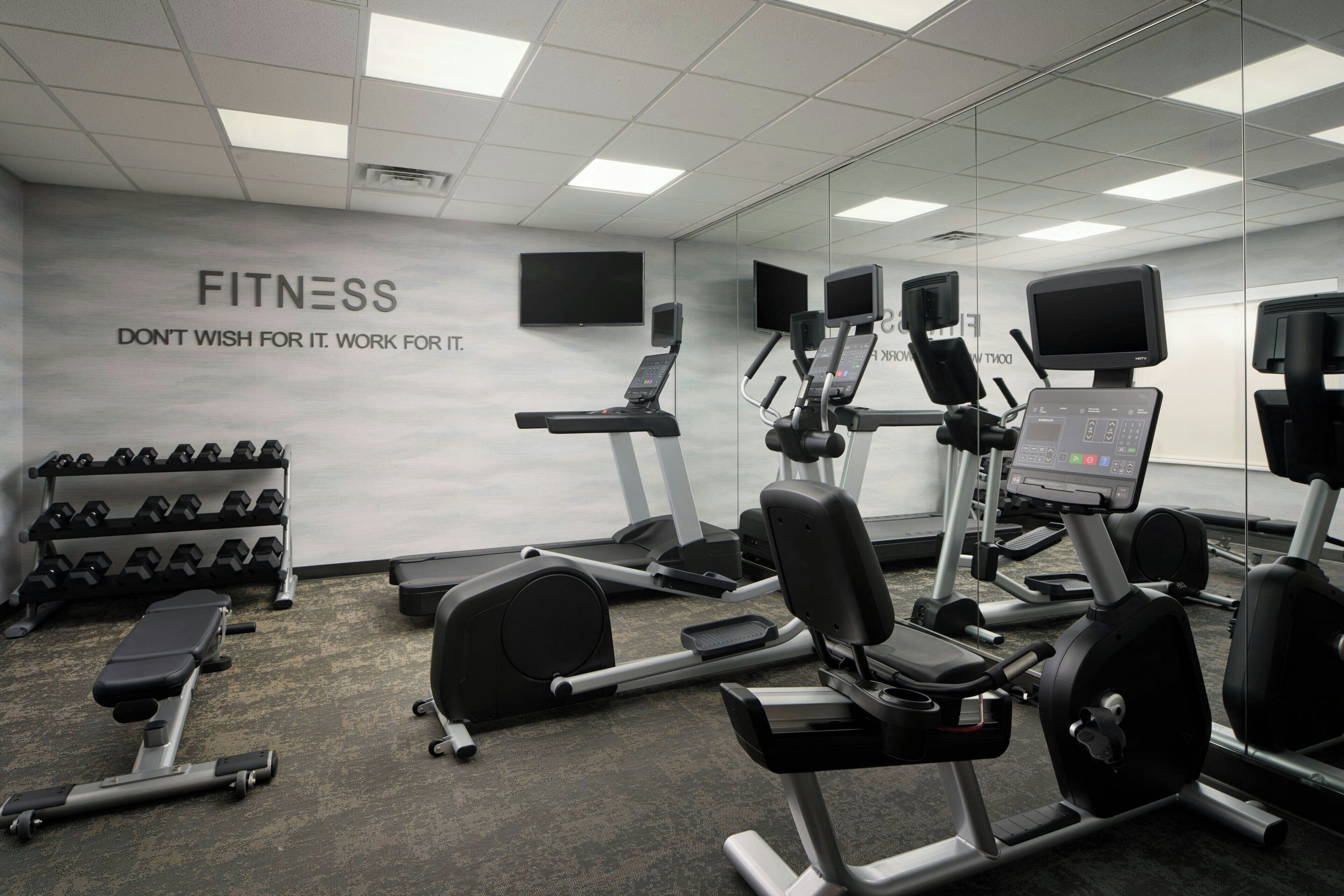 Une salle de sport équipée de matériel d’exercice, d’un téléviseur fixé au mur et d’une citation inspirante.