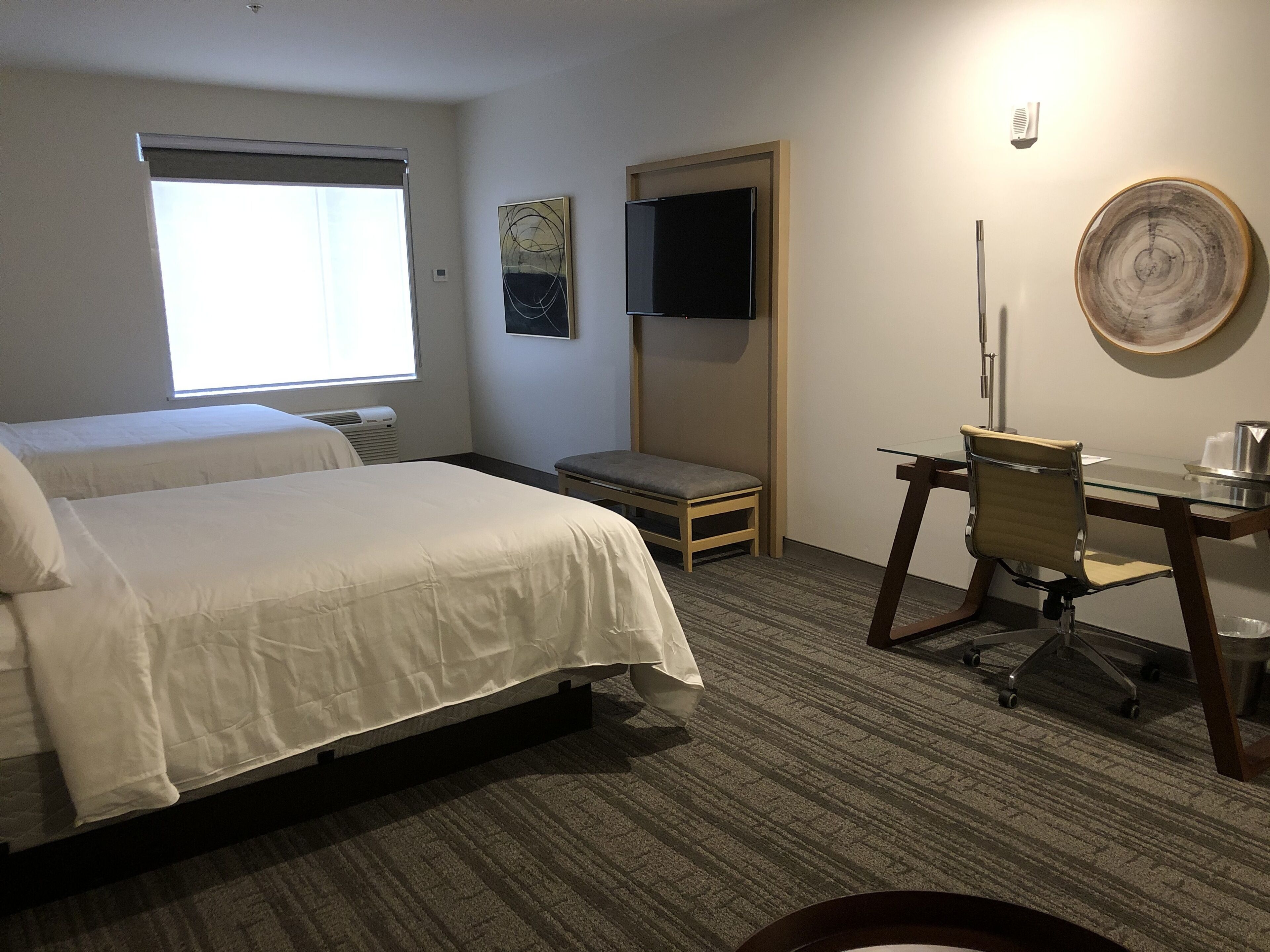 A hotel room with two beds, a desk with a chair, a television, and a large window.