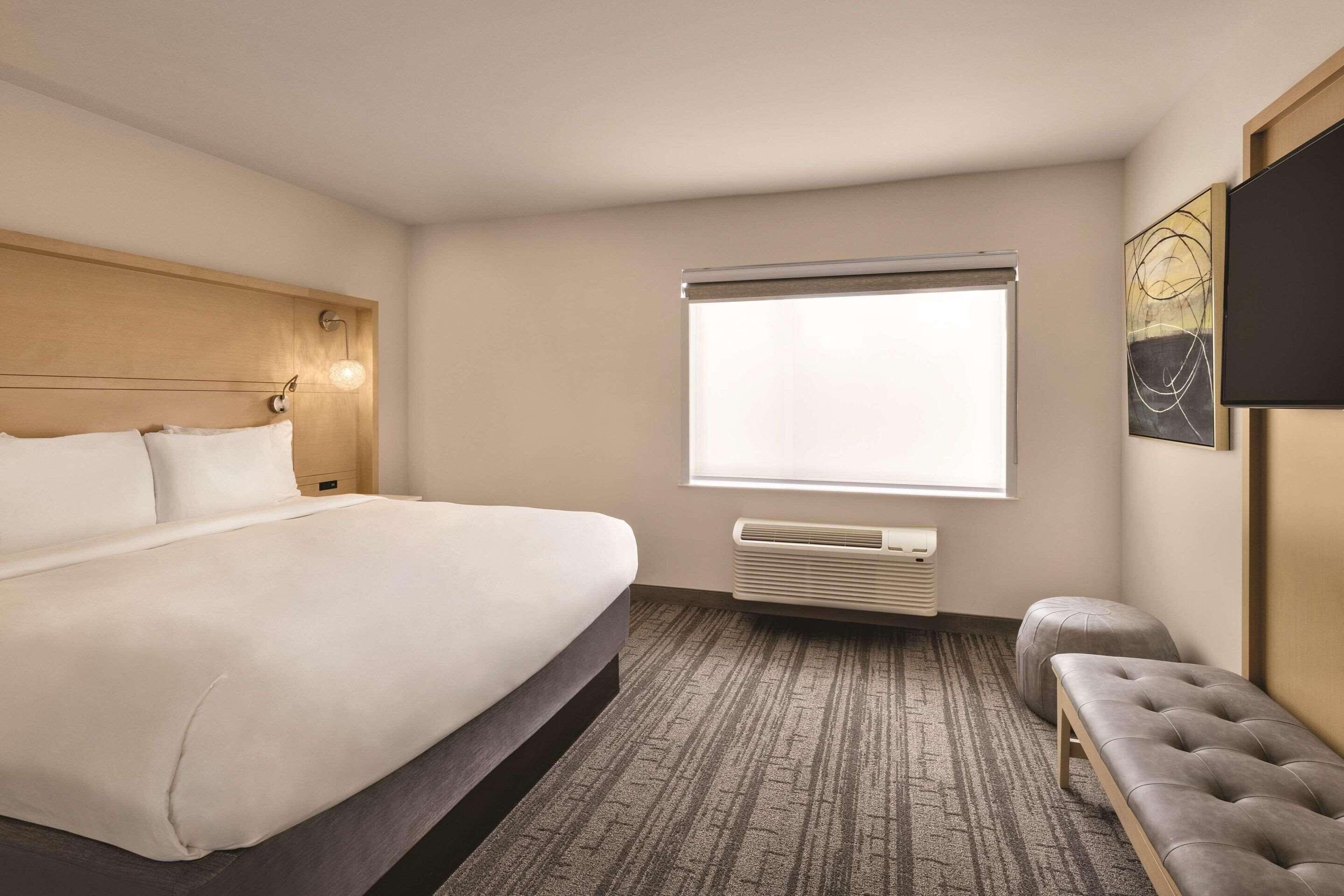 Hotelkamer met een groot bed, een bankje, een televisie aan de muur en een raam met zonwering.