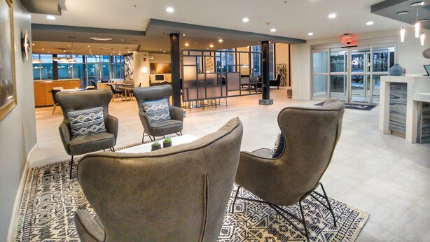 A spacious lobby with modern furniture, a reception desk, and a view of the outside through large windows. - Radisson Hotel Atlanta Airport (College Park)