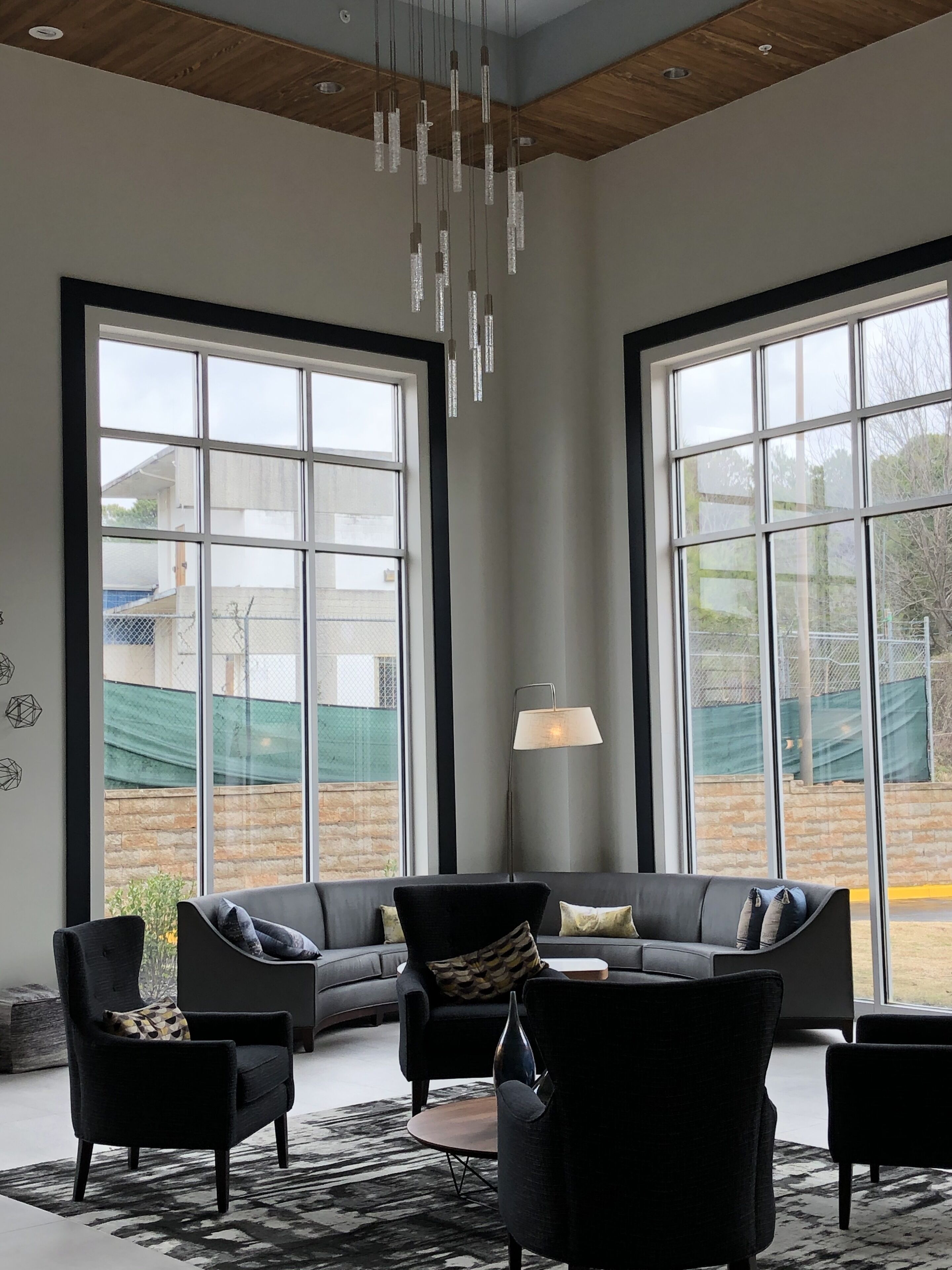 Uma sala de estar moderna com grandes janelas, um sofá preto, um abajur de chão e um lustre.