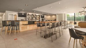 A modern kitchen with a bar area, featuring a wooden countertop, black bar stools, and pendant lighting. - Radisson Hotel Atlanta Airport (College Park)