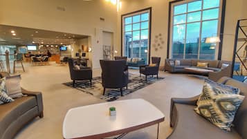Een ruime lobby met een modern design, met een zithoek met banken en fauteuils, een salontafel en grote ramen met uitzicht op de stad.