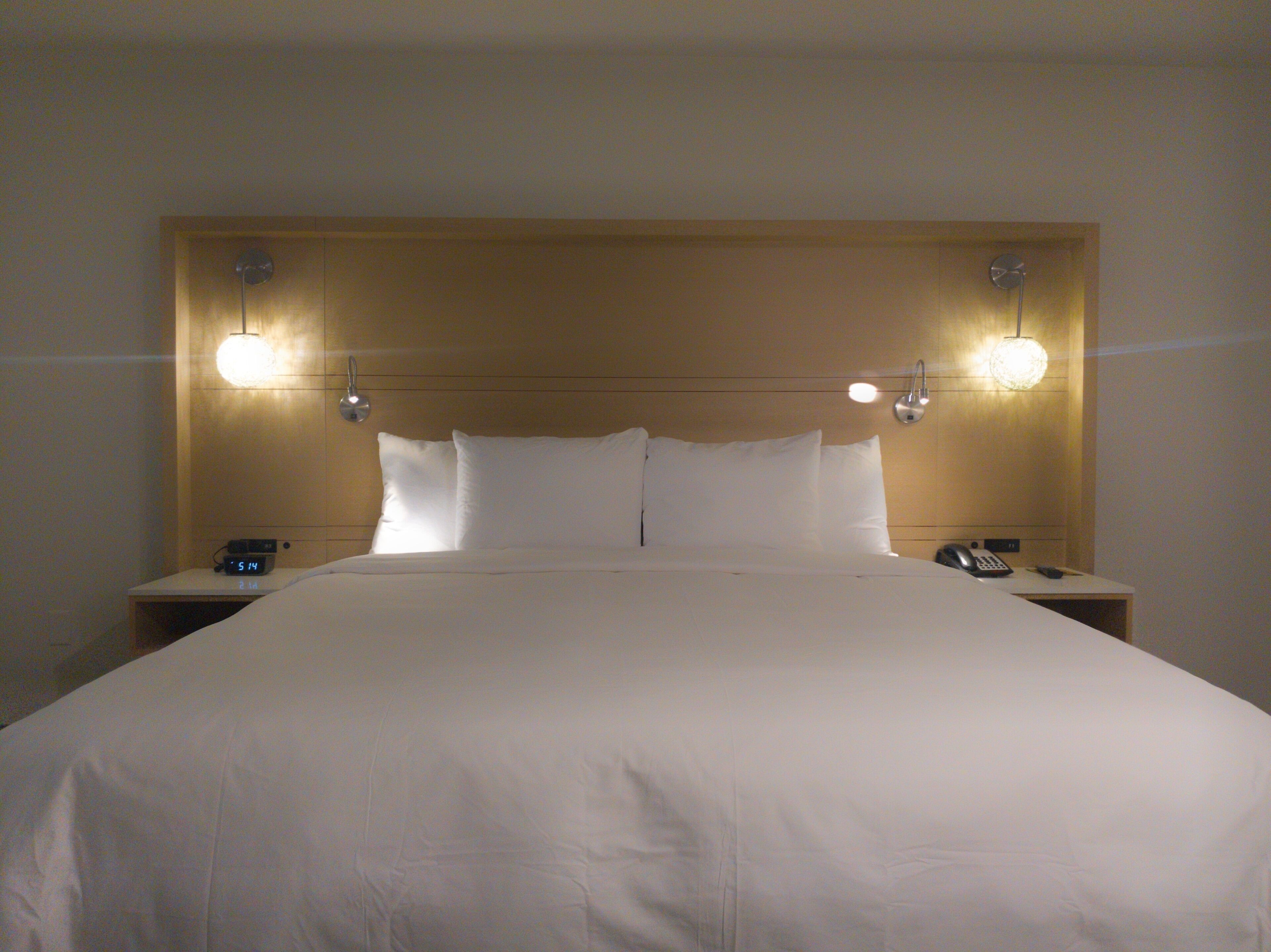 A neatly made bed with white linens, two bedside tables with lamps, and a clock on one table.