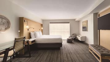 Una habitación de hotel con cama, escritorio, silla, televisor y un ventanal grande.