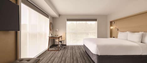 A hotel room with a large bed, a desk, a chair, and a bench.
