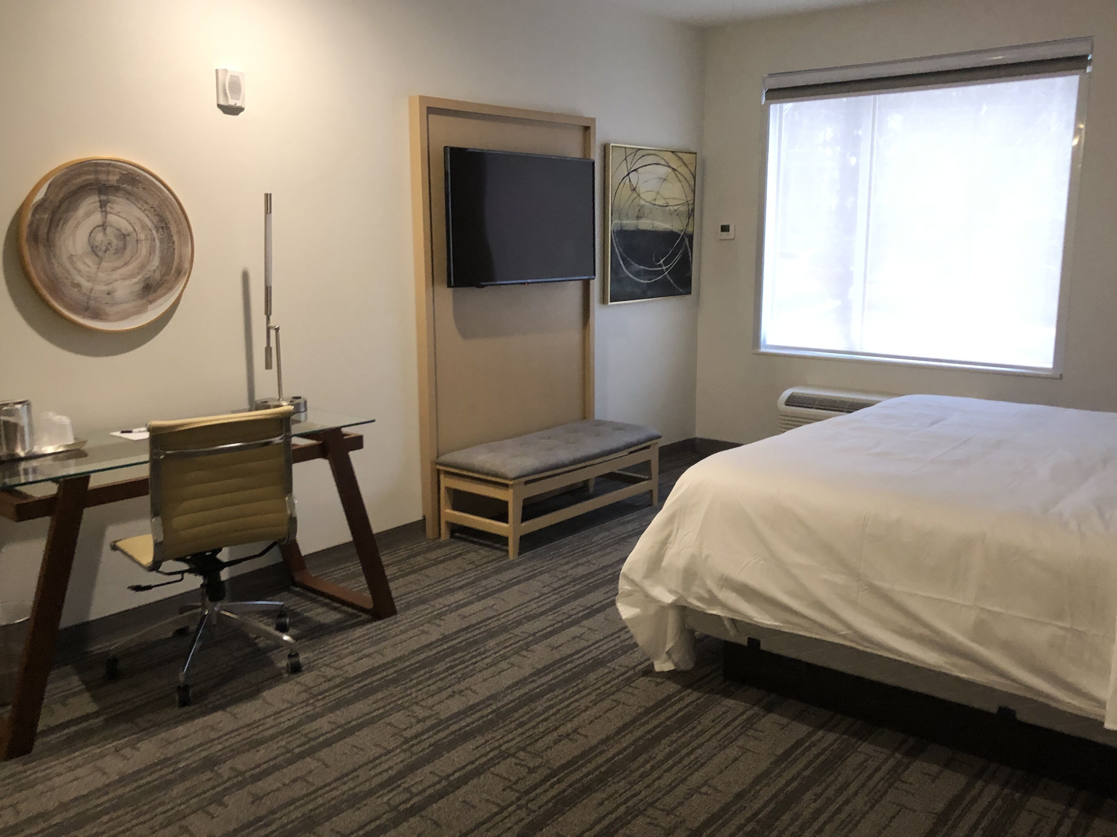 A hotel room with a bed, a desk with a chair, a television, and a window.