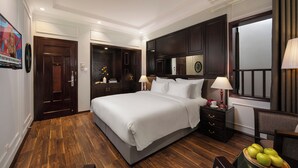 A hotel room with a large bed, dark wooden flooring, a nightstand with a lamp, a small table with apples, and a TV mounted on the wall. - Hong Ngoc Dynastie Boutique Hotel & Spa (Hanoi)