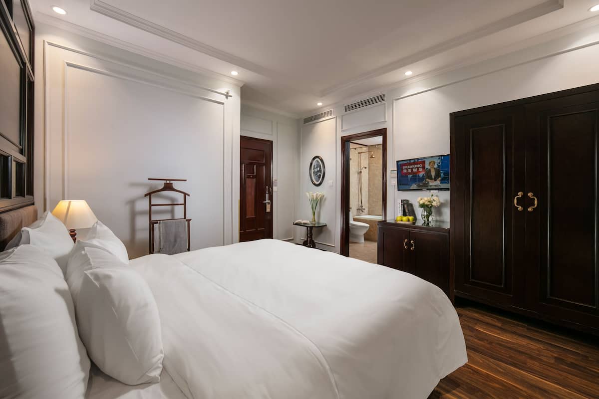 Relax in a spacious room with a large, neatly made bed, a wooden wardrobe, and a wall-mounted TV.