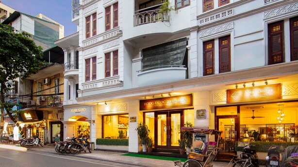 A multi-story building with a restaurant named "HONG NGOC DYNASTLE" on the ground floor. There are several motorcycles parked in front, and the building features traditional architectural elements with decorative moldings and wooden shutters. - Hong Ngoc Dynastie Boutique Hotel & Spa (Hanoi)