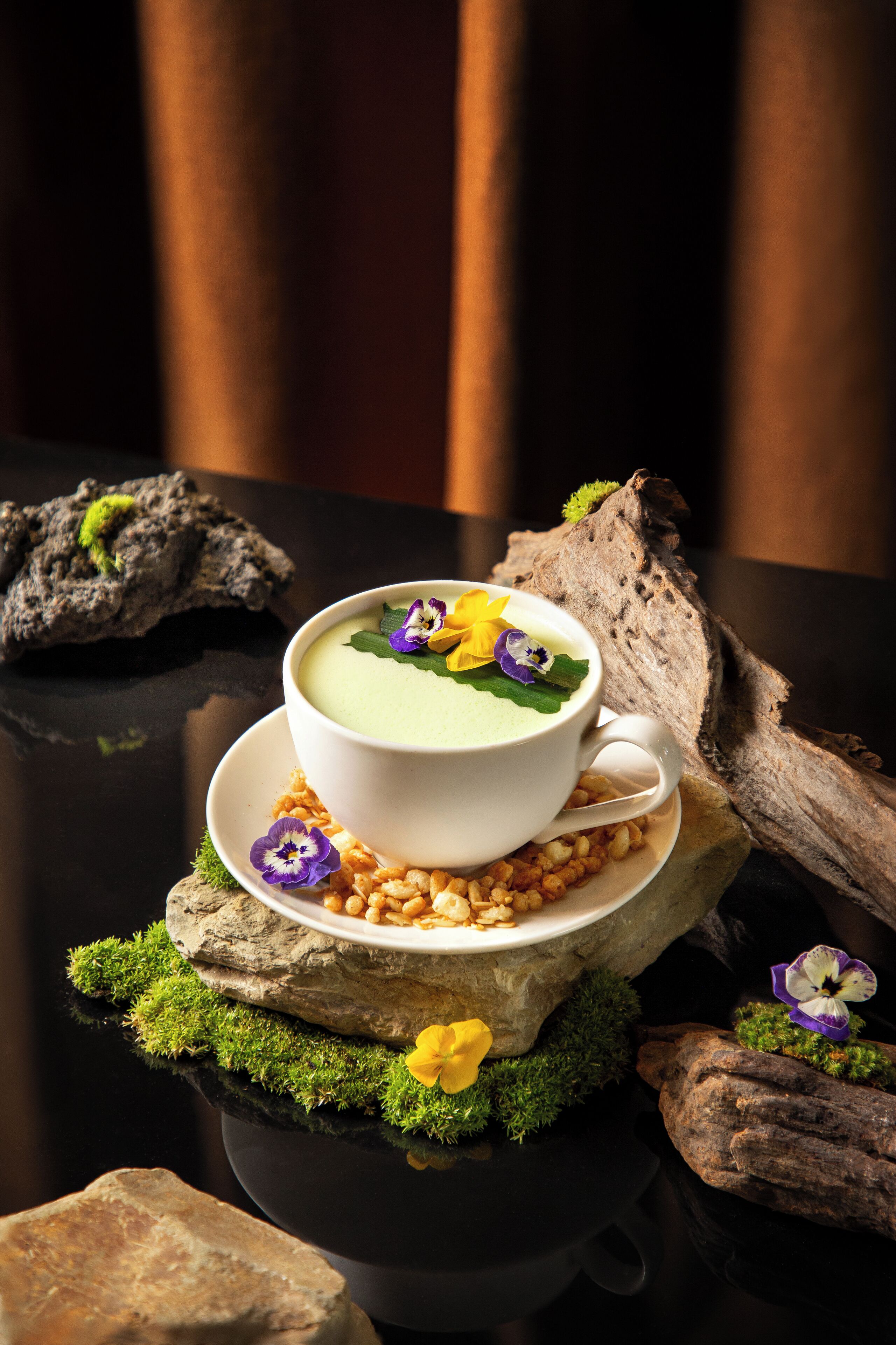 A white cup of soup on a moss-covered rock with a rustic background.