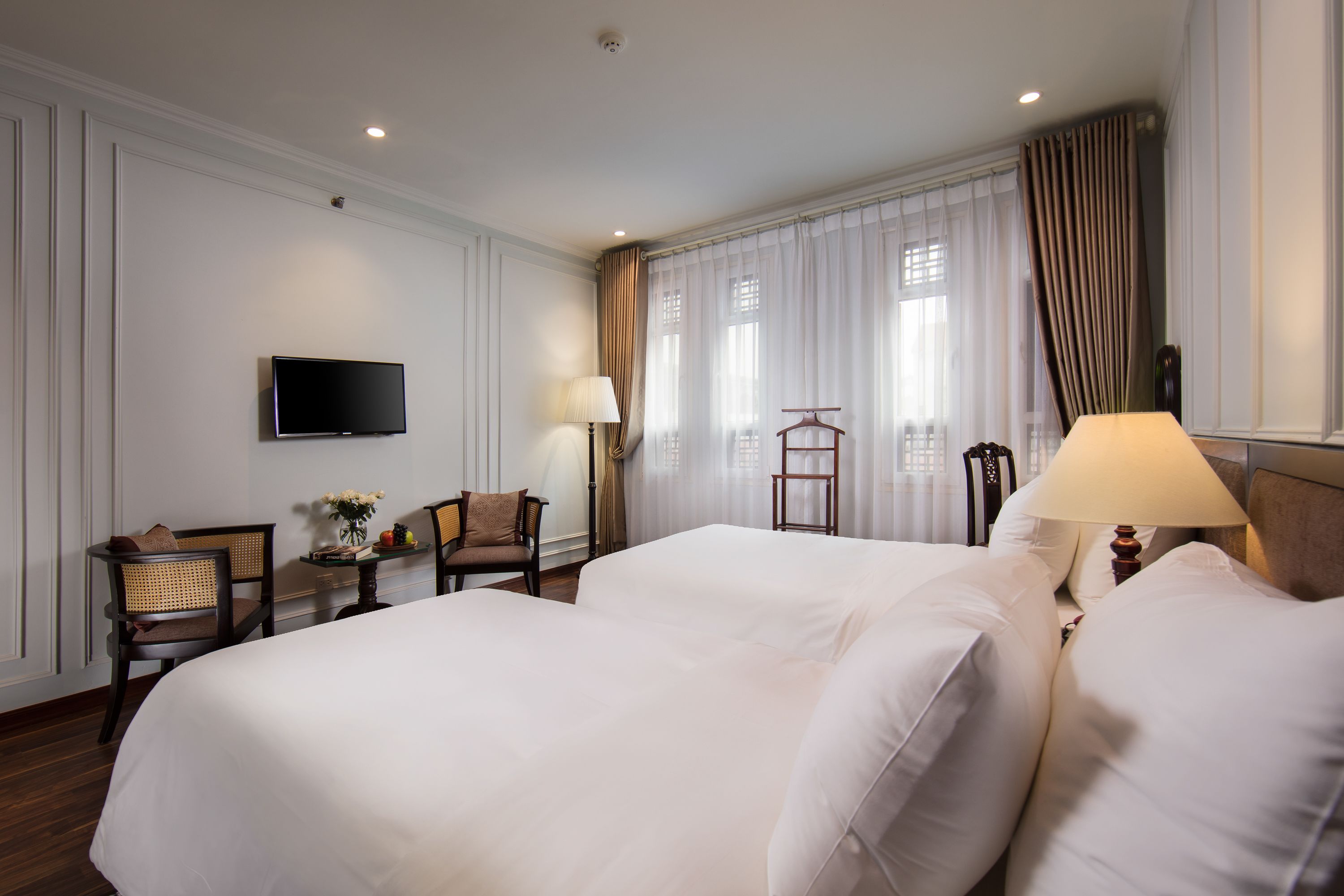 A hotel room with two beds, a television, a desk with a lamp, and a chair.