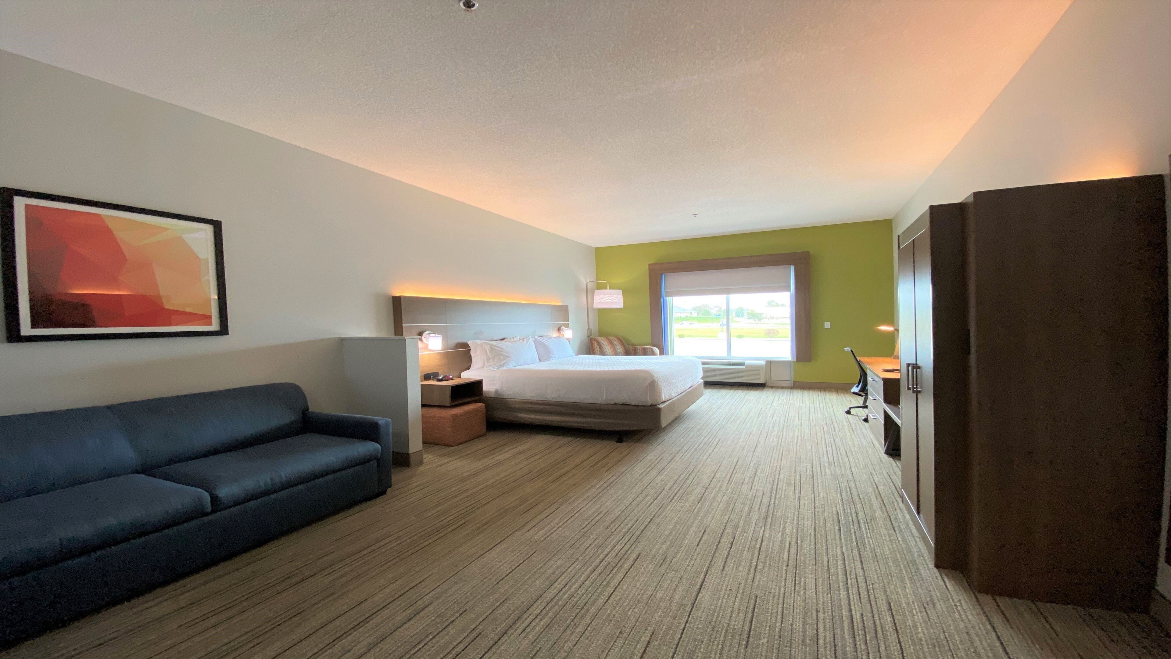 A hotel room with a bed, a desk, a chair, a sofa, and a window.