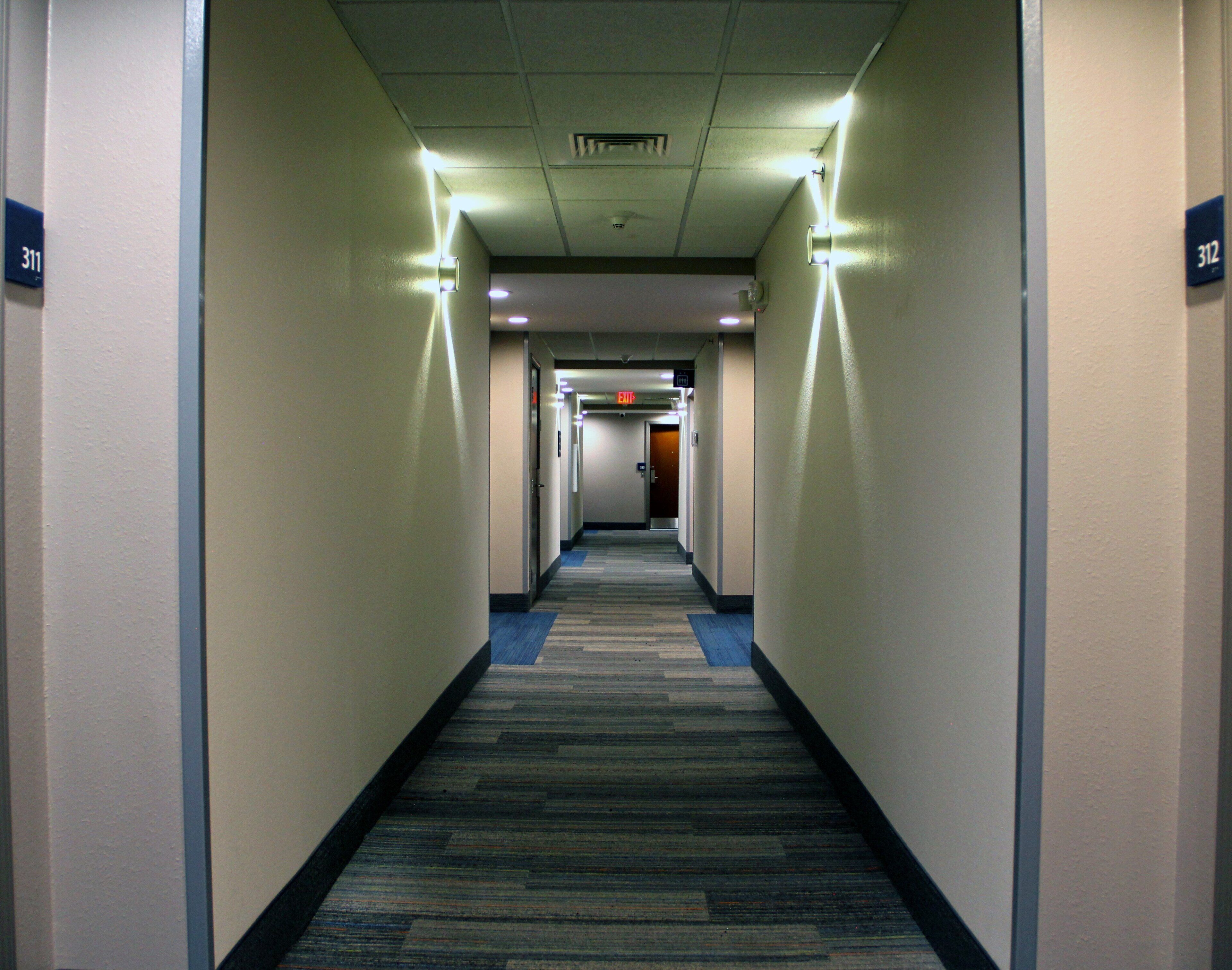 Un couloir d’hôtel avec des revêtements de sol en moquette, des murs ornés d’indications de numéros de chambres et un panneau indiquant la sortie.
