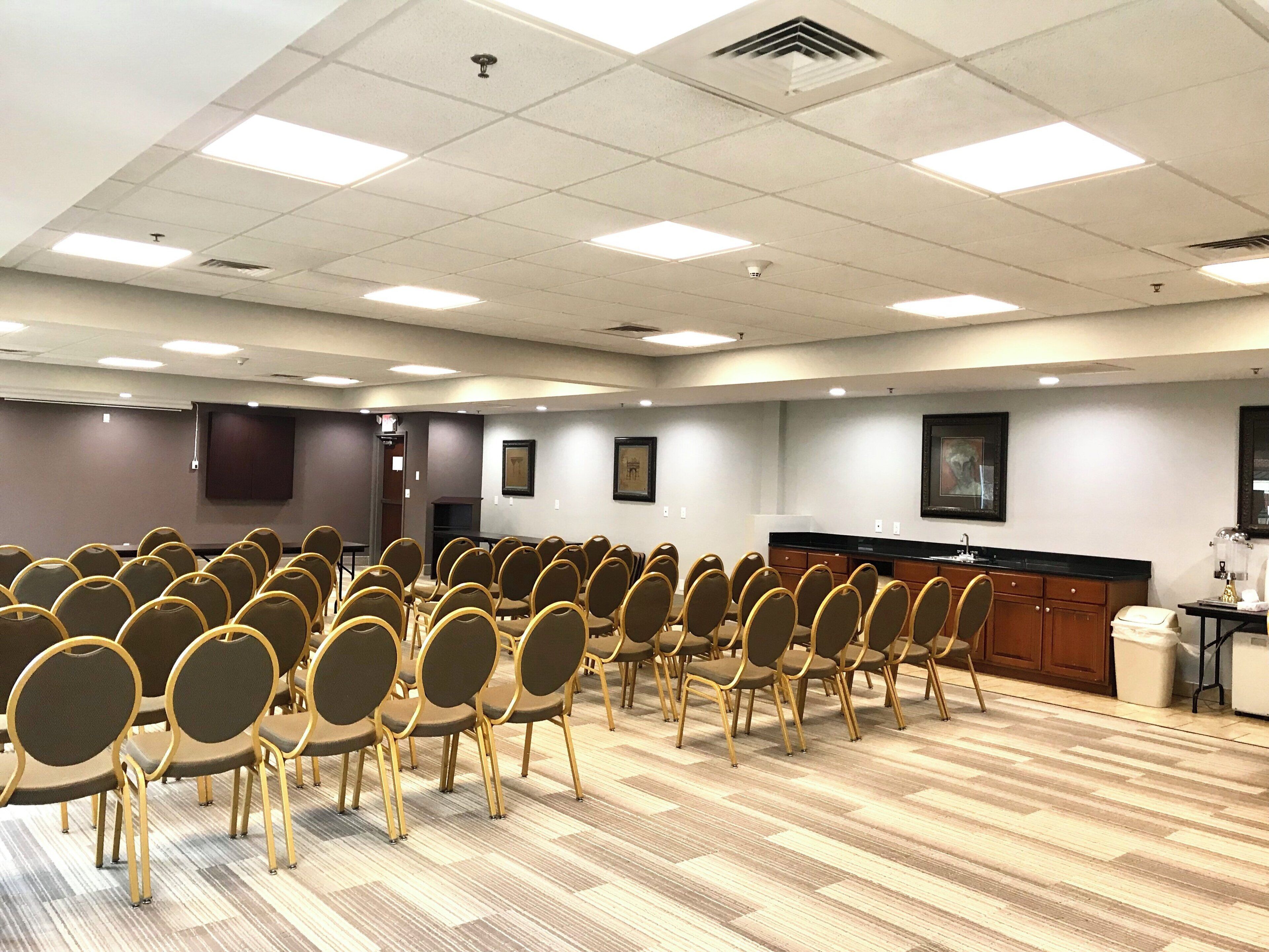 A conference room with rows of chairs, a podium, and a large screen.