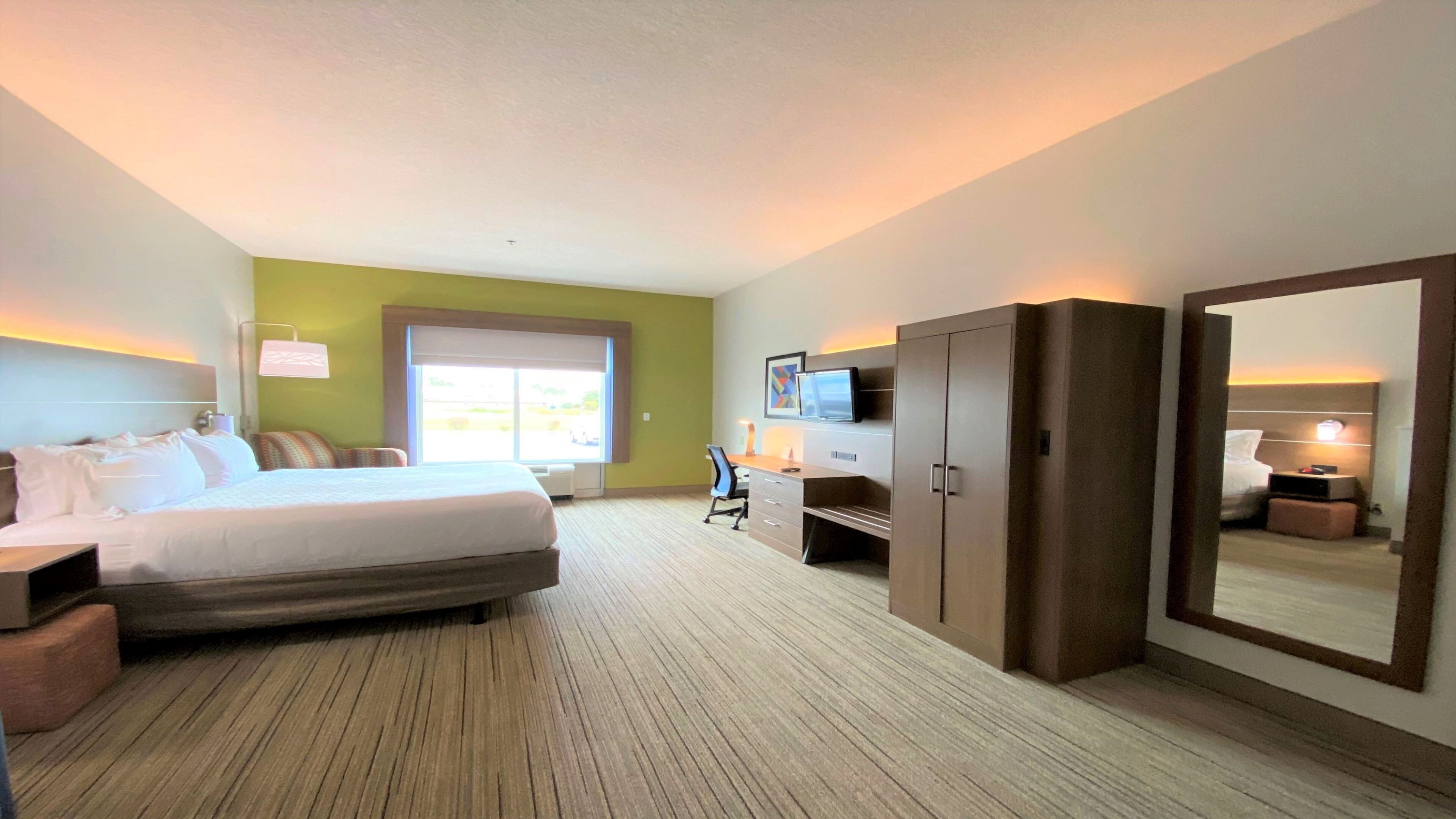 Ein Hotelzimmer mit Bett, Schreibtisch, Stuhl, Kleiderschrank und einem großen Spiegel.
