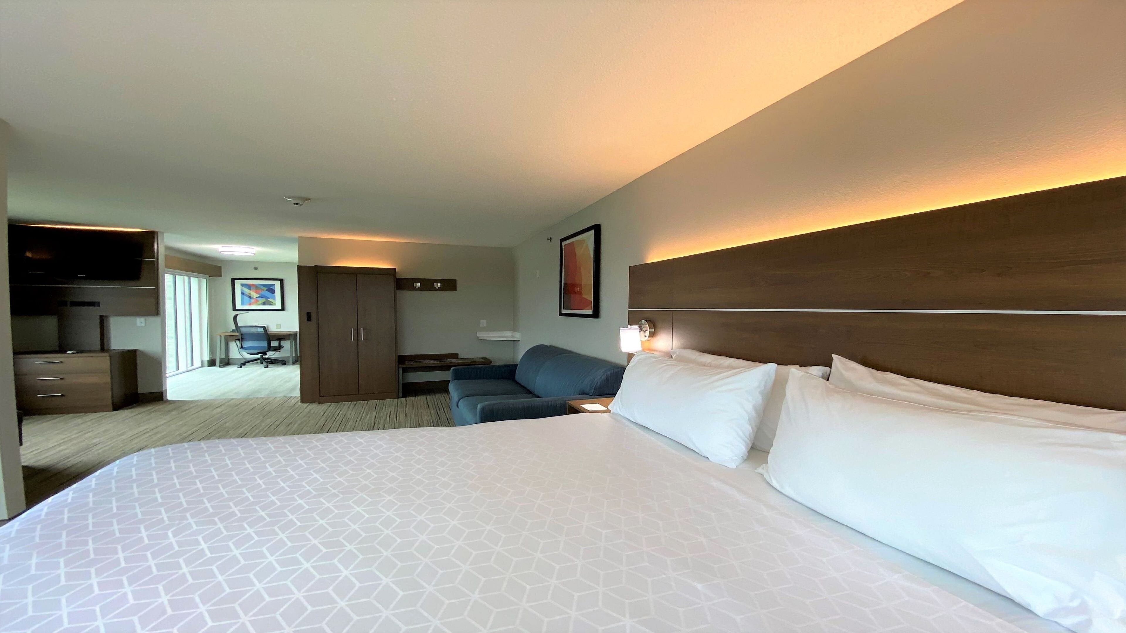 A hotel room with a large bed, a desk, a chair, and a wardrobe.