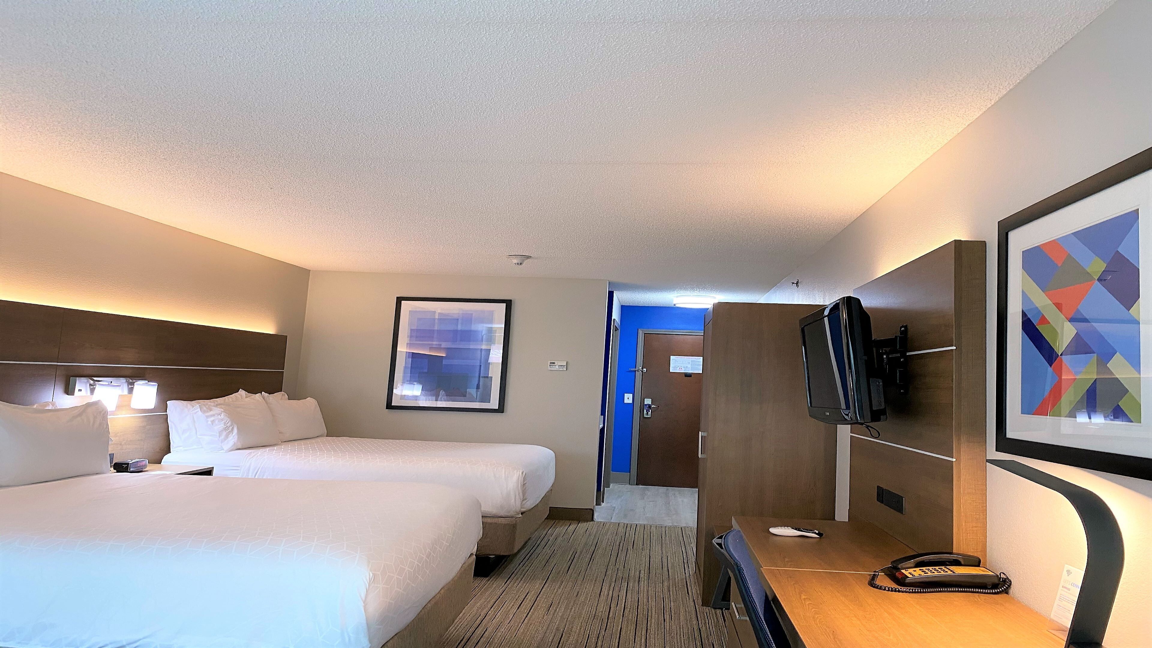 Habitación de hotel con dos camas, un escritorio con teléfono, un televisor montado en la pared y una puerta que da a otra habitación.