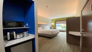 A hotel room with a bed, a desk with a microwave, a coffee maker, and a window with a view of the outside.