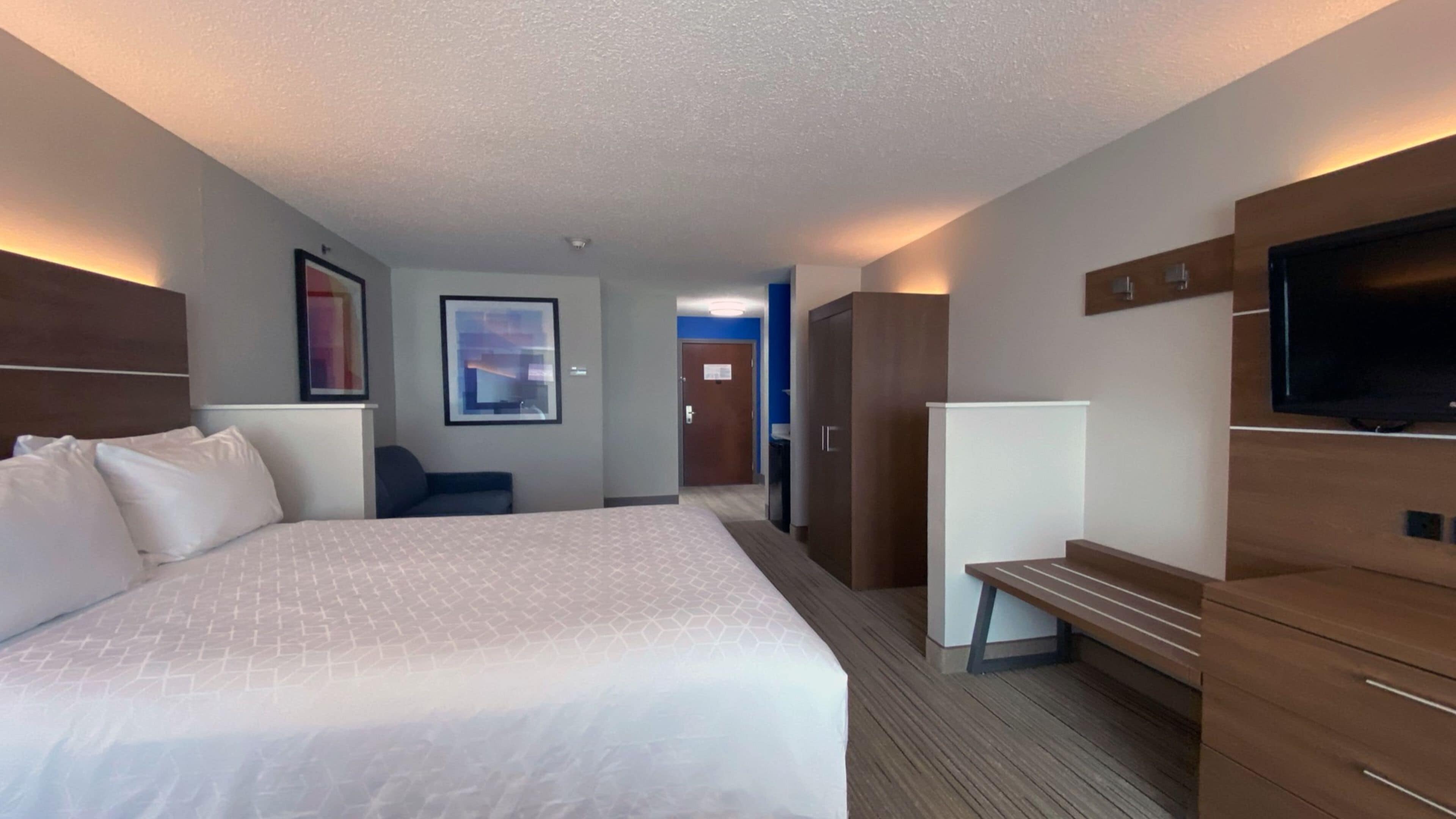 Una habitación de hotel con una cama grande, un escritorio, una silla, un armario y un televisor.