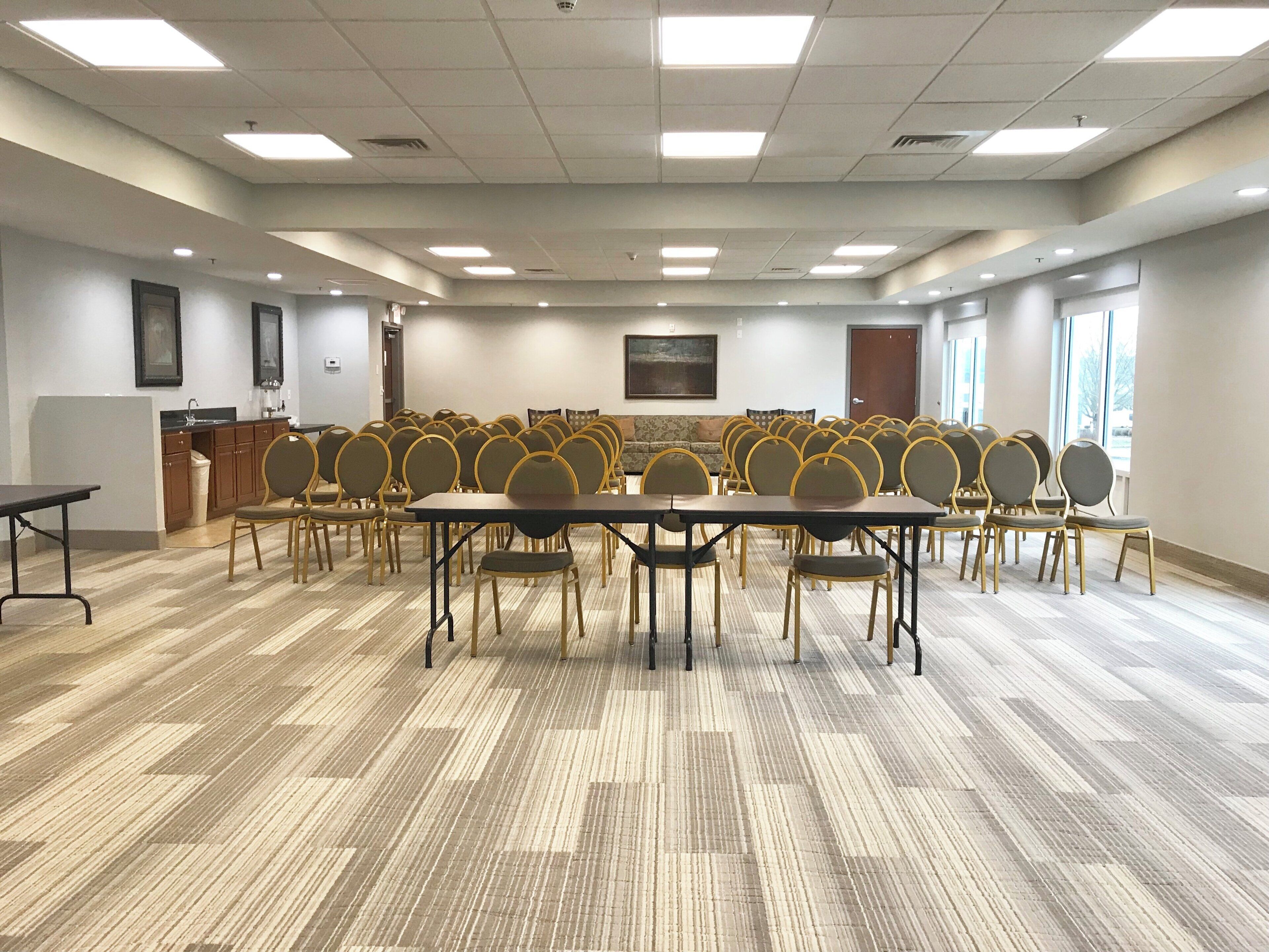 A conference room with multiple tables and chairs, a kitchenette, and a large window.