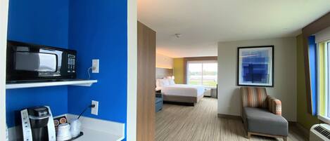 A hotel room with a kitchenette, a bed, a seating area, and a large window.