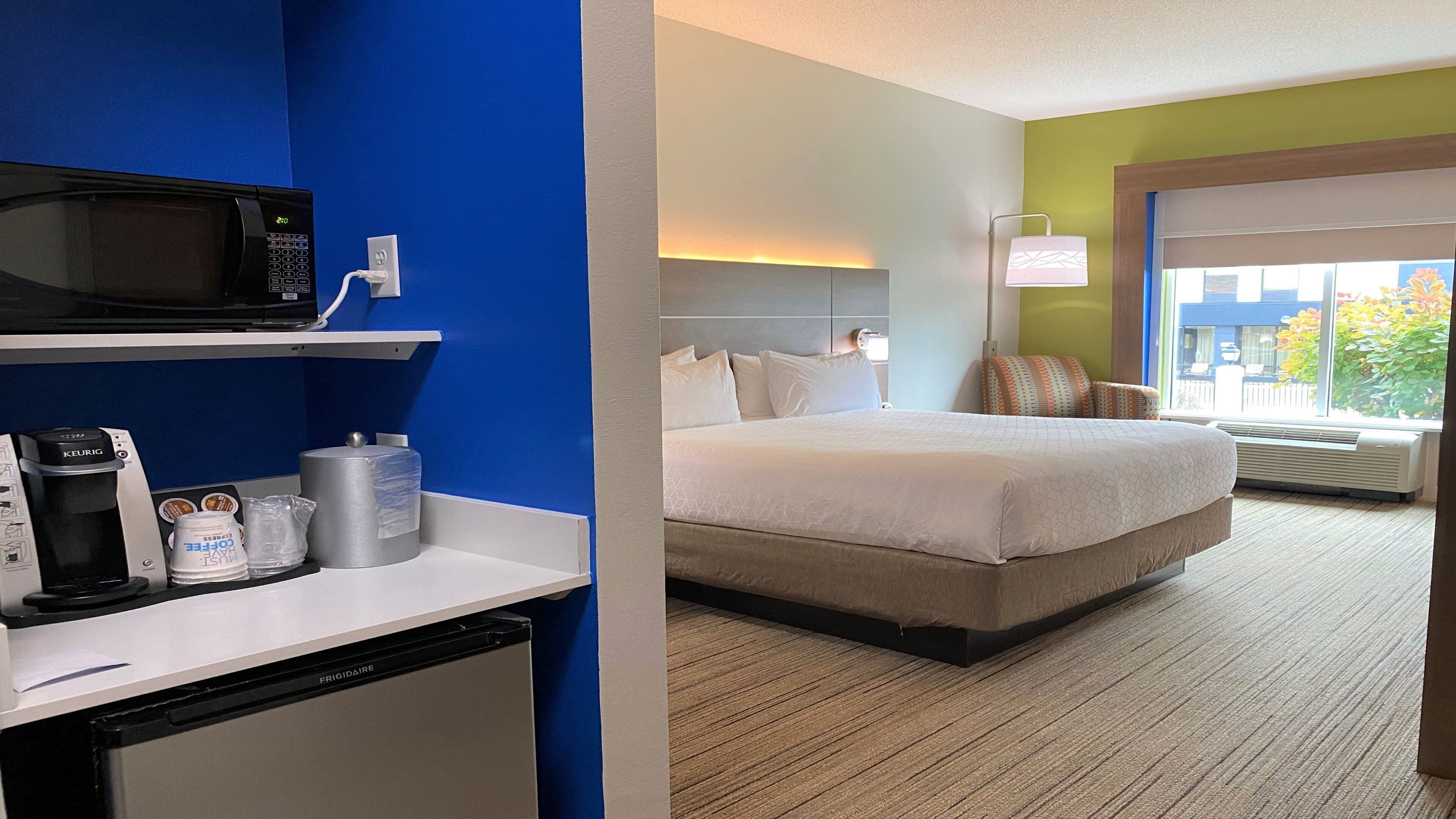 Habitación de hotel con una cama, un escritorio con cafetera, un microondas y ventana con vistas.