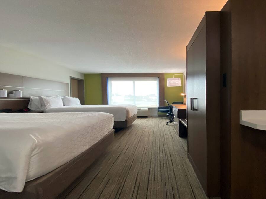Habitación de hotel con dos camas, un escritorio, una silla, un ventanal y un minibar.