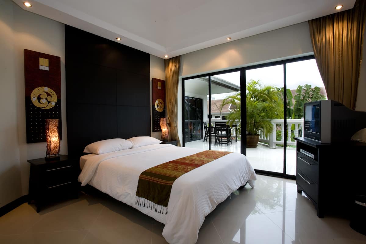 A modern hotel bedroom with a large bed, a TV, and a balcony with a view of greenery.