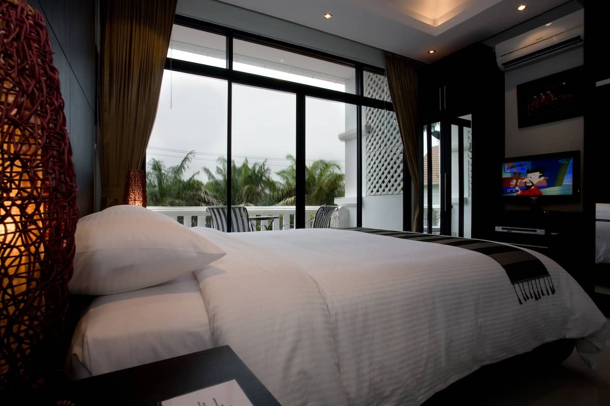 A hotel room with a large bed, a TV, and a view of palm trees through the window.
