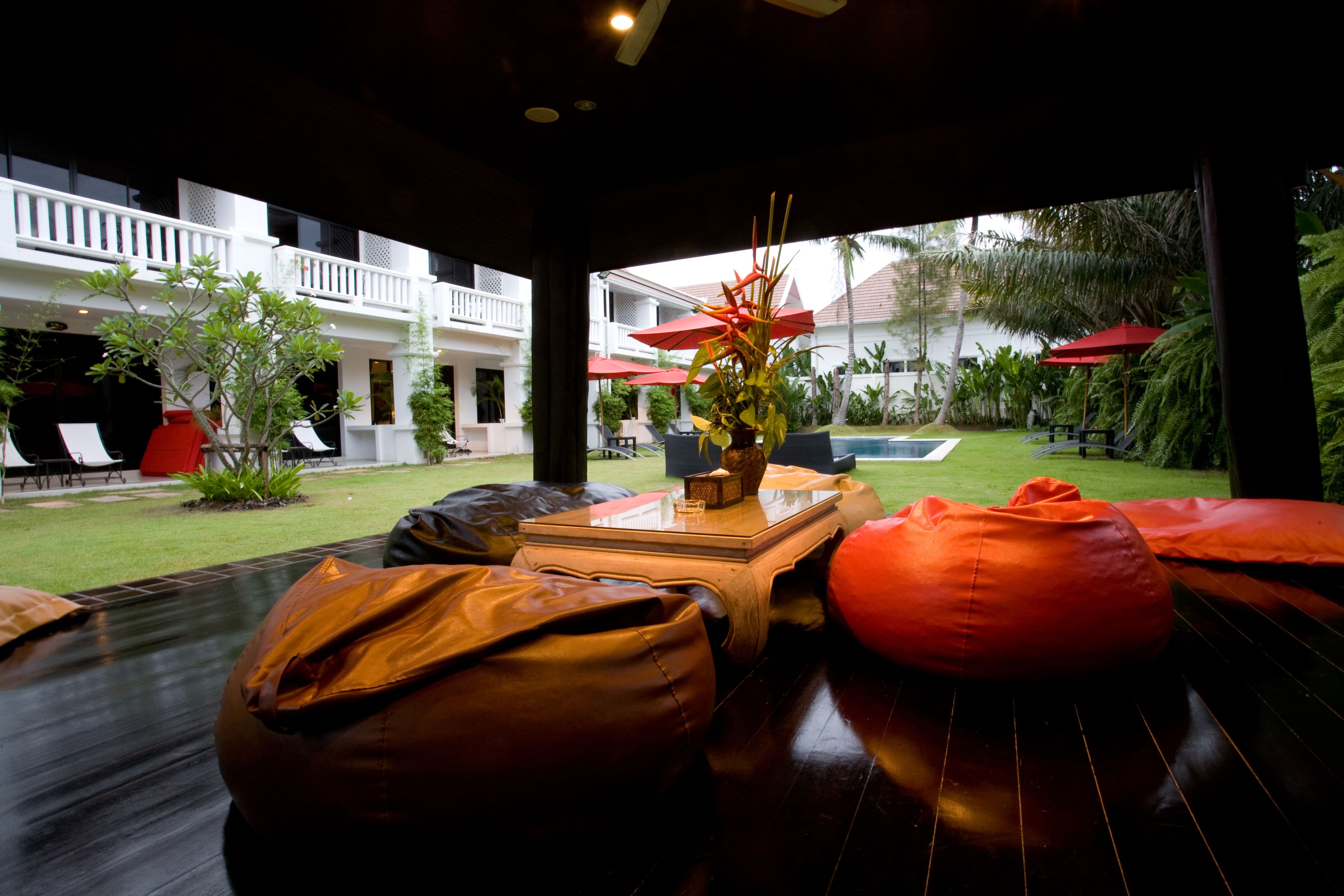 A modern outdoor seating area with wooden tables and orange bean bags, overlooking a pool and lush greenery.