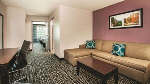 Quarto de hotel com sofá, mesa de centro, mesa de jantar e cadeiras, e carpete estampado.