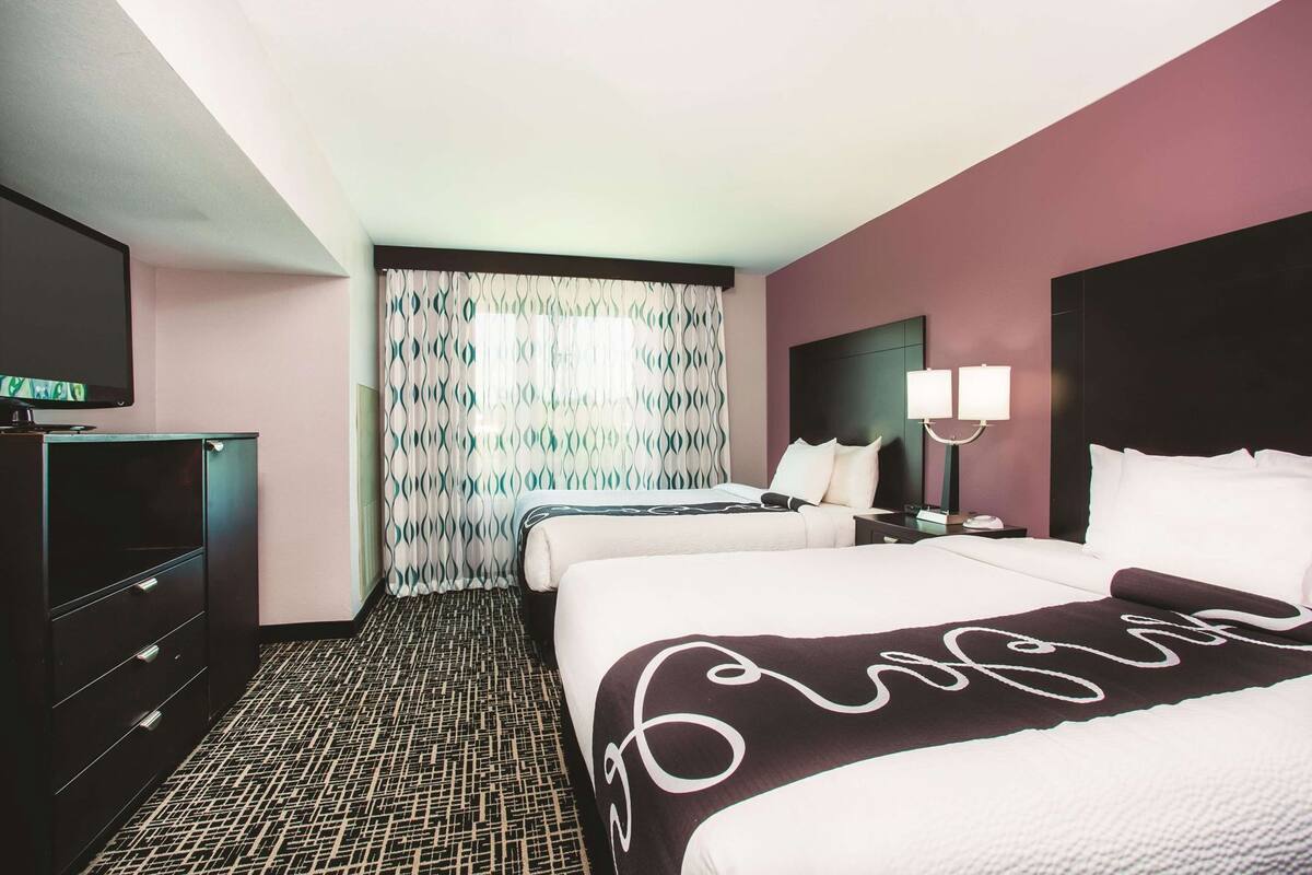 Una habitación de hotel con dos camas, televisión, cortina estampada y piso con diseño.