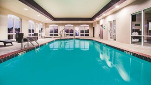Uma piscina interior com água cristalina, uma cadeira de salva-vidas e uma escada de piscina.