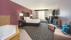 Quarto de hotel com uma cama grande, área de estar com sofá e poltrona, escrivaninha e uma banheira espaçosa.