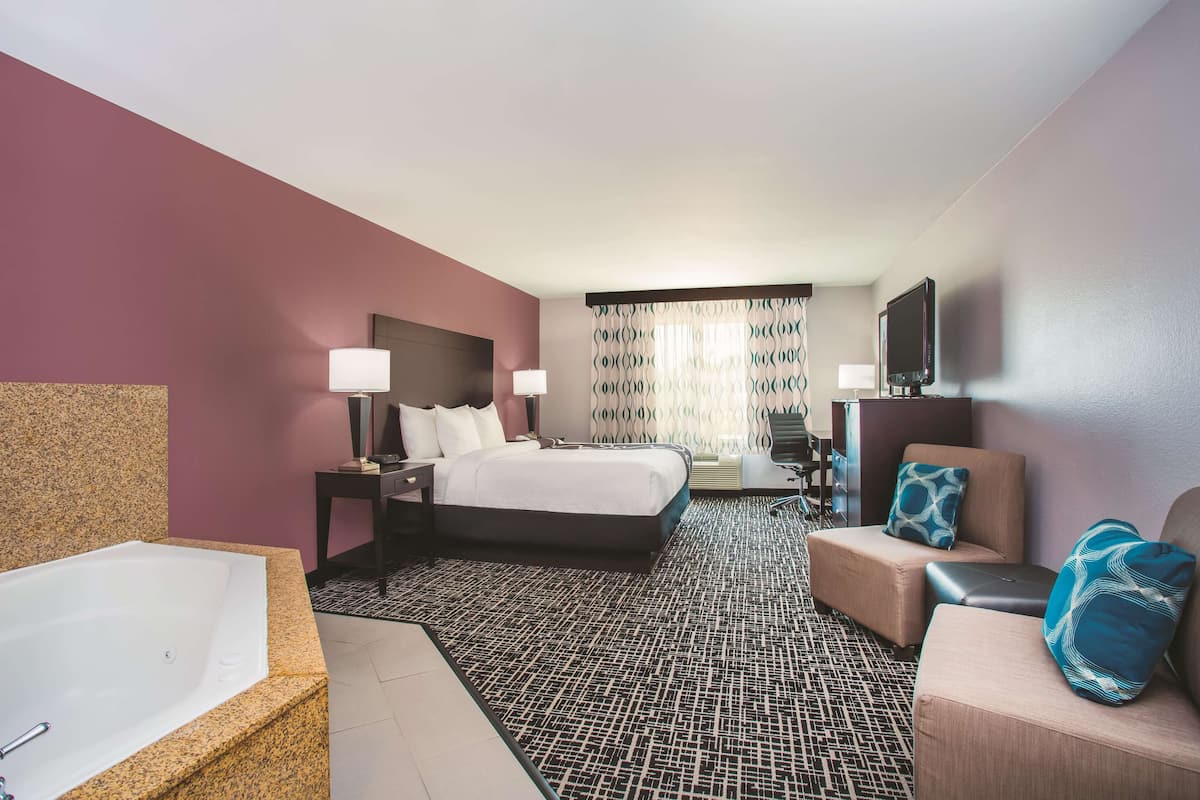 Una habitación de hotel con una cama grande, una zona de estar con sofá y sillón, un escritorio y una bañera amplia.