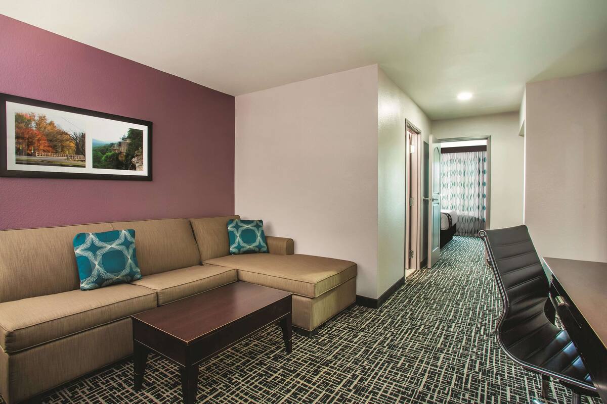 Habitación de hotel con sofá, una mesita de centro, suelo estampado, una mesa de conferencias y un cuadro en la pared.