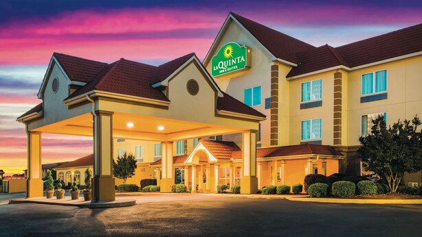 Um hotel com entrada coberta, uma placa indicando "La Quinta Inn & Suites" e fachada bem iluminada.