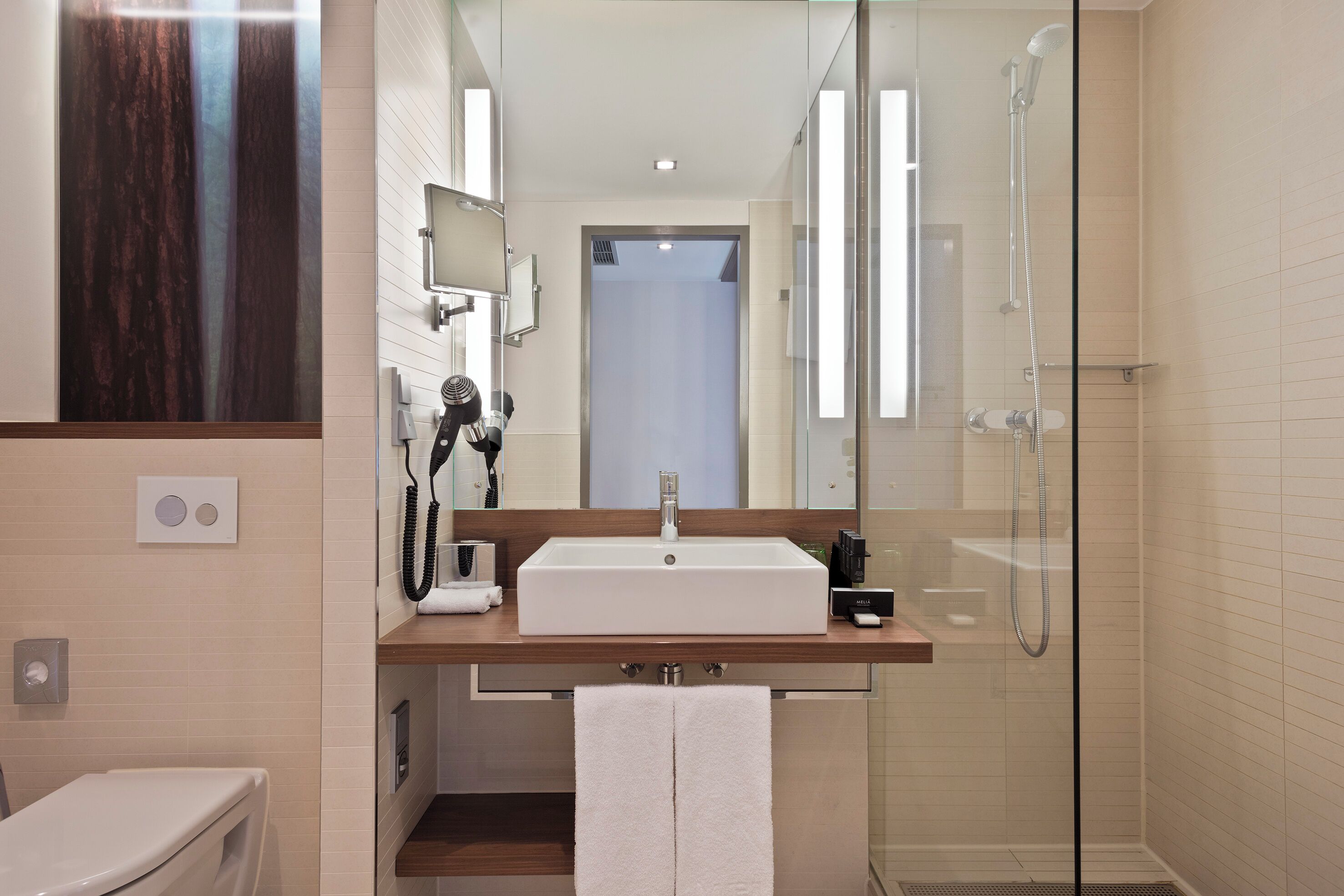 A modern bathroom with a large mirror, a sink, and a glass-enclosed shower.