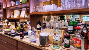 Zona de bar con diversas botellas de alcohol, vasos y un cartel que anuncia una hora feliz de cócteles.