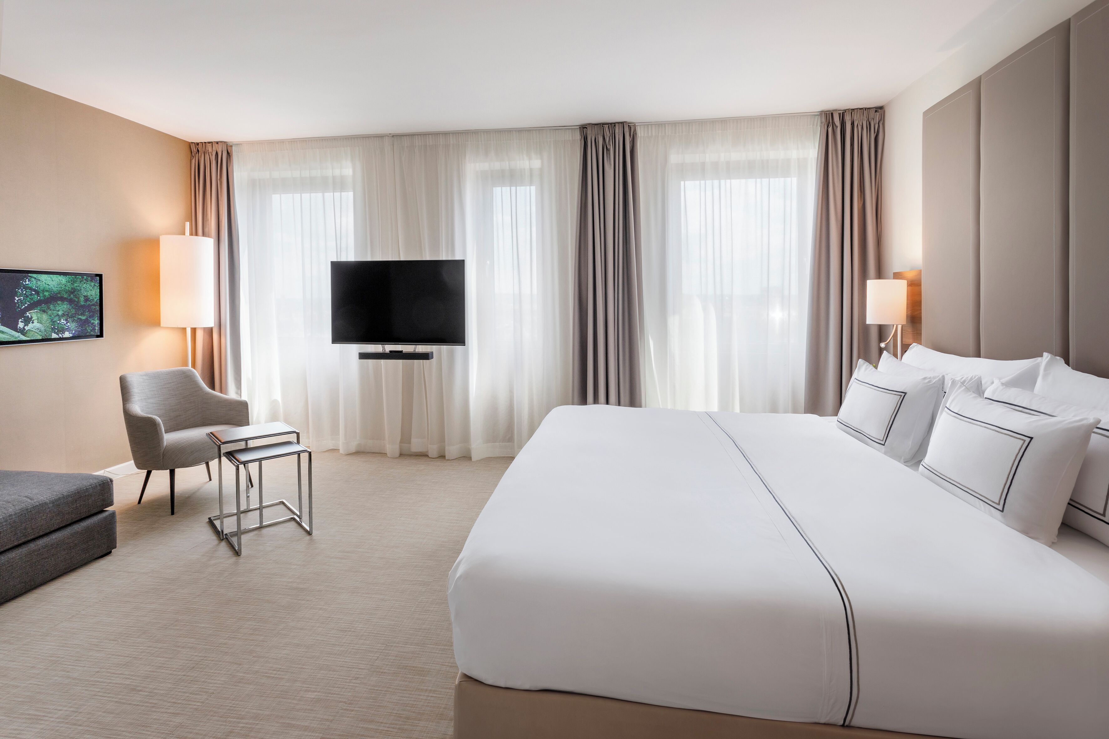 Quarto de hotel com uma cama grande, televisão de tela plana, escrivaninha, poltrona e sofá.