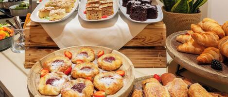 A buffet with various pastries and desserts, including cakes, brownies, and croissants.