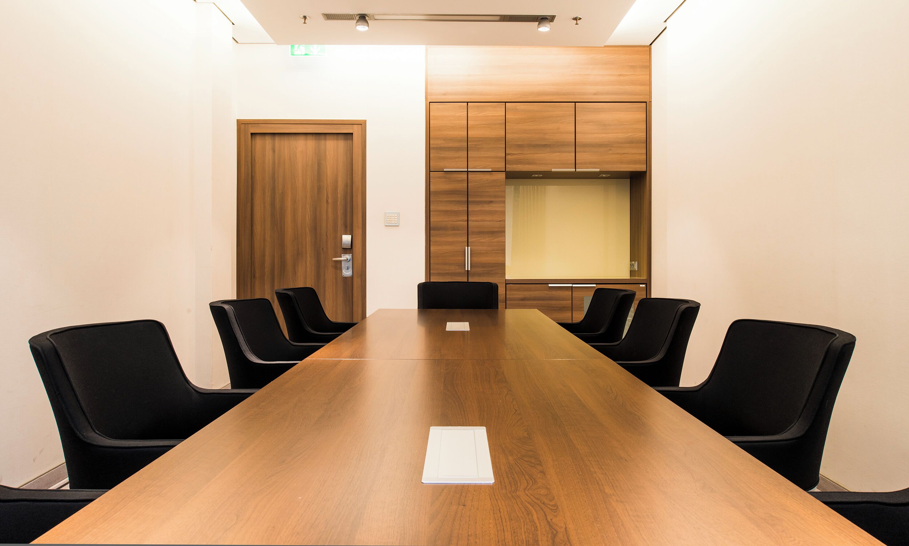 A conference room with a long wooden table, black chairs, and wooden cabinets.