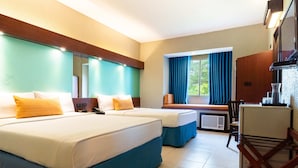 A hotel room with two beds, a desk, a chair, a mirror, and a window with curtains. - Microtel by Wyndham Eagle Ridge (General Trias)