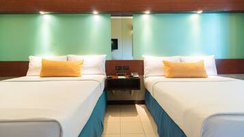 Habitación de hotel con dos camas, cada una con ropa blanca y una almohada amarilla. Entre las camas hay una mesita de noche de madera con un teléfono y una lámpara pequeña.