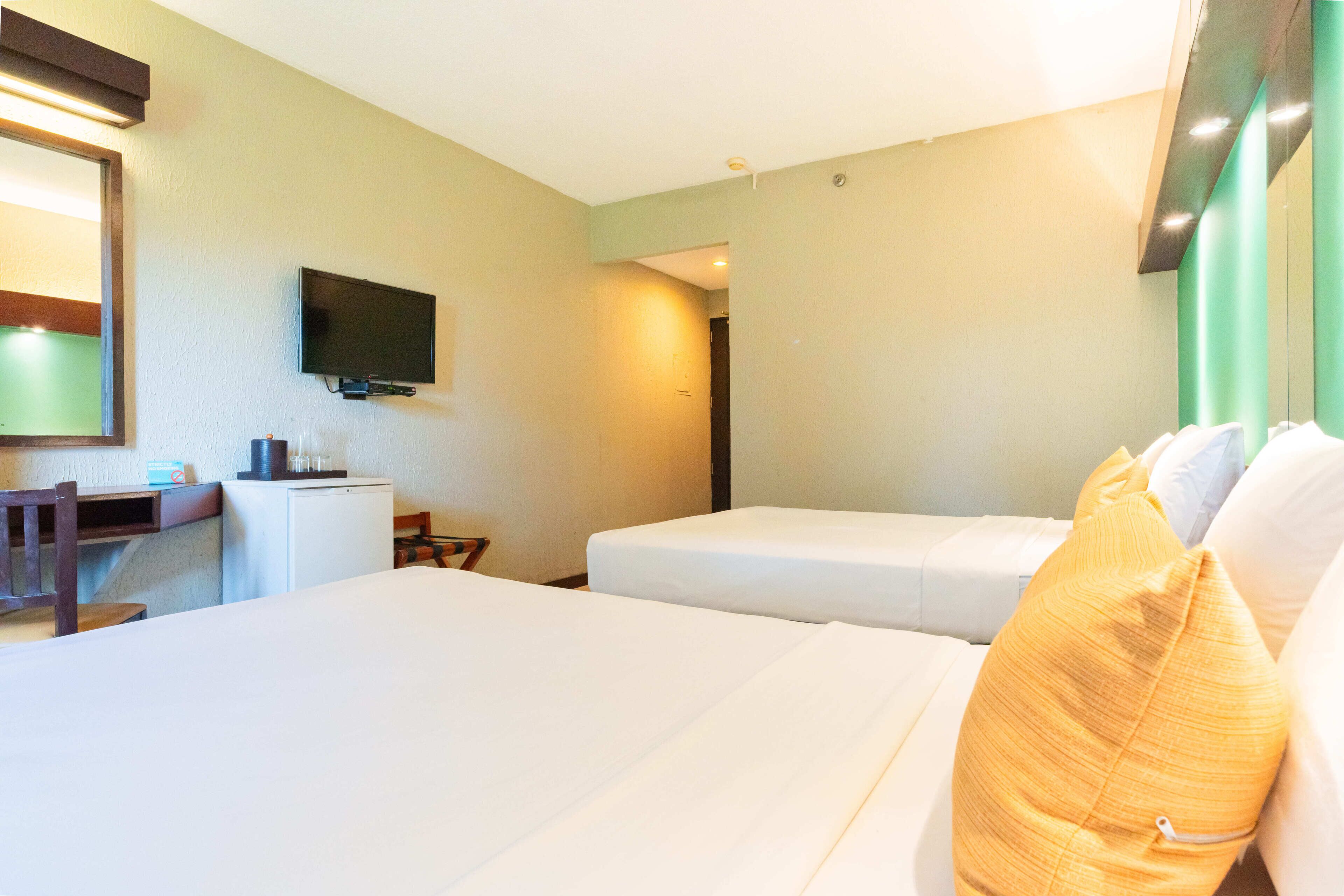 A hotel room with two beds, a desk, a television, and a mirror.