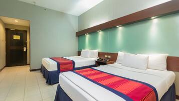 A hotel room with two beds, a wooden headboard, a nightstand, and a door leading to another room.