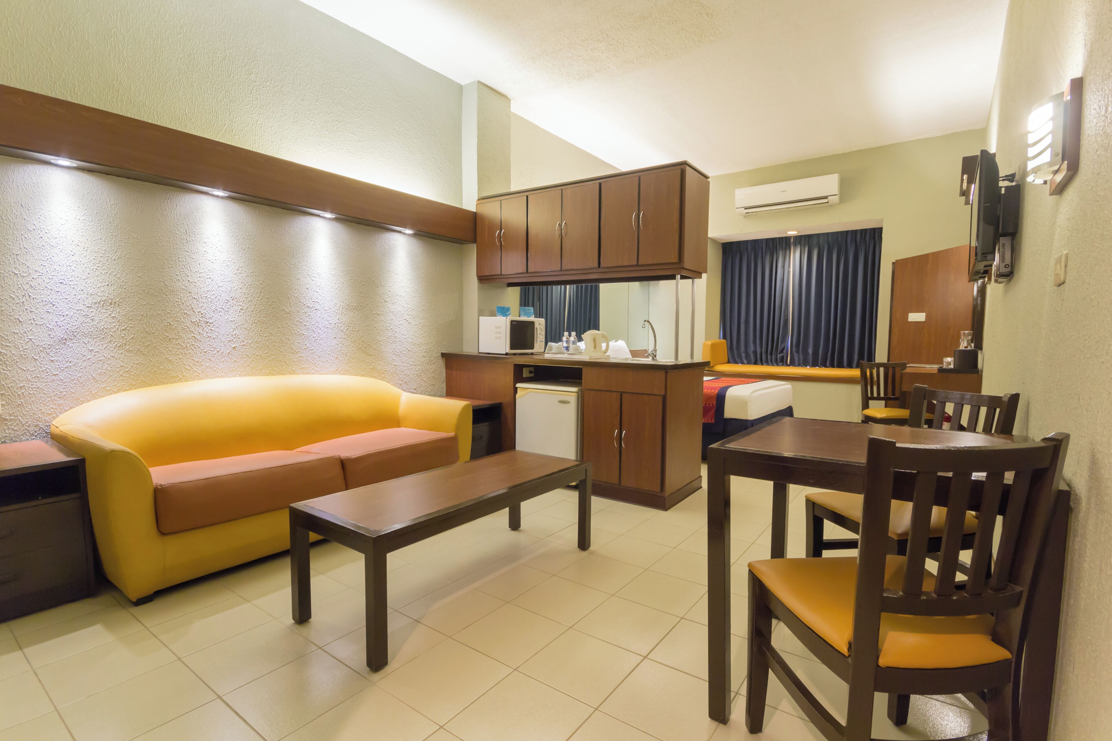 A compact living space with a sofa, a dining table, a kitchen area, and a TV mounted on the wall.